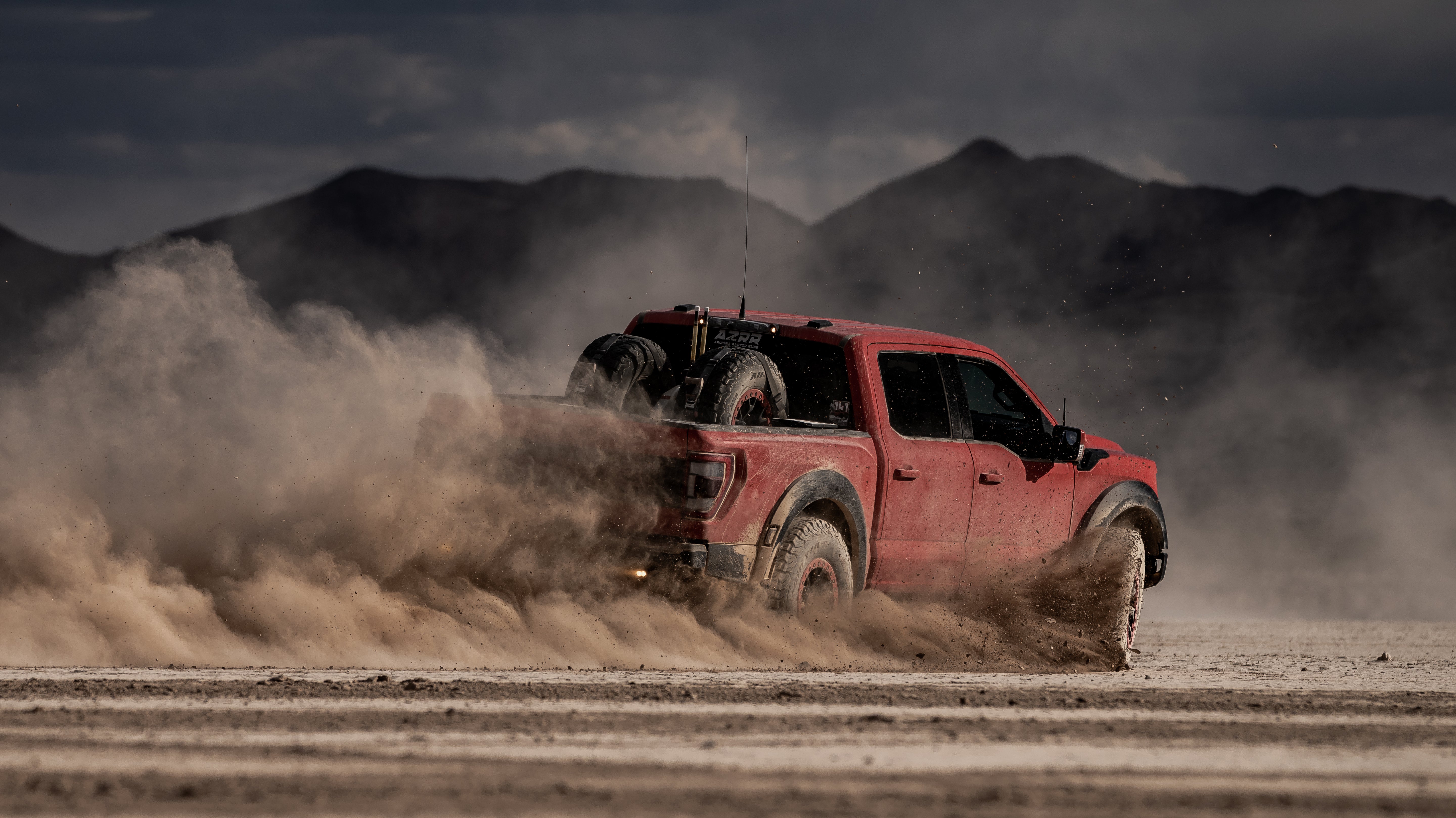 Red truck driving on a dirt road with HSM bed link mount