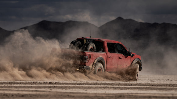 Red truck driving on a dirt road with HSM bed link mount